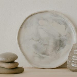 Artistic display of a ceramic plate and vase with stacked stones, showcasing minimalist aesthetics.